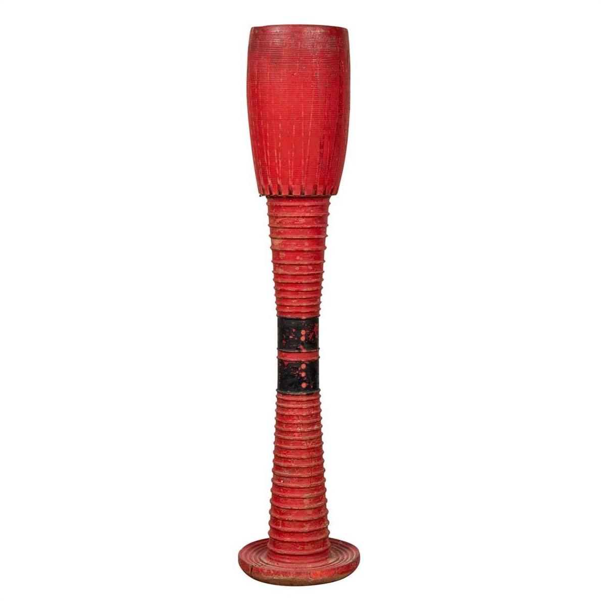 Red wood ceremonial drum with round base, ridged sides, and black central band shown freestanding.