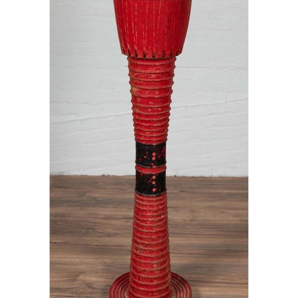 Red ribbed ceramic vase with round base, tall design, inspired by Antique Thai ceremonial drums, on plain background.