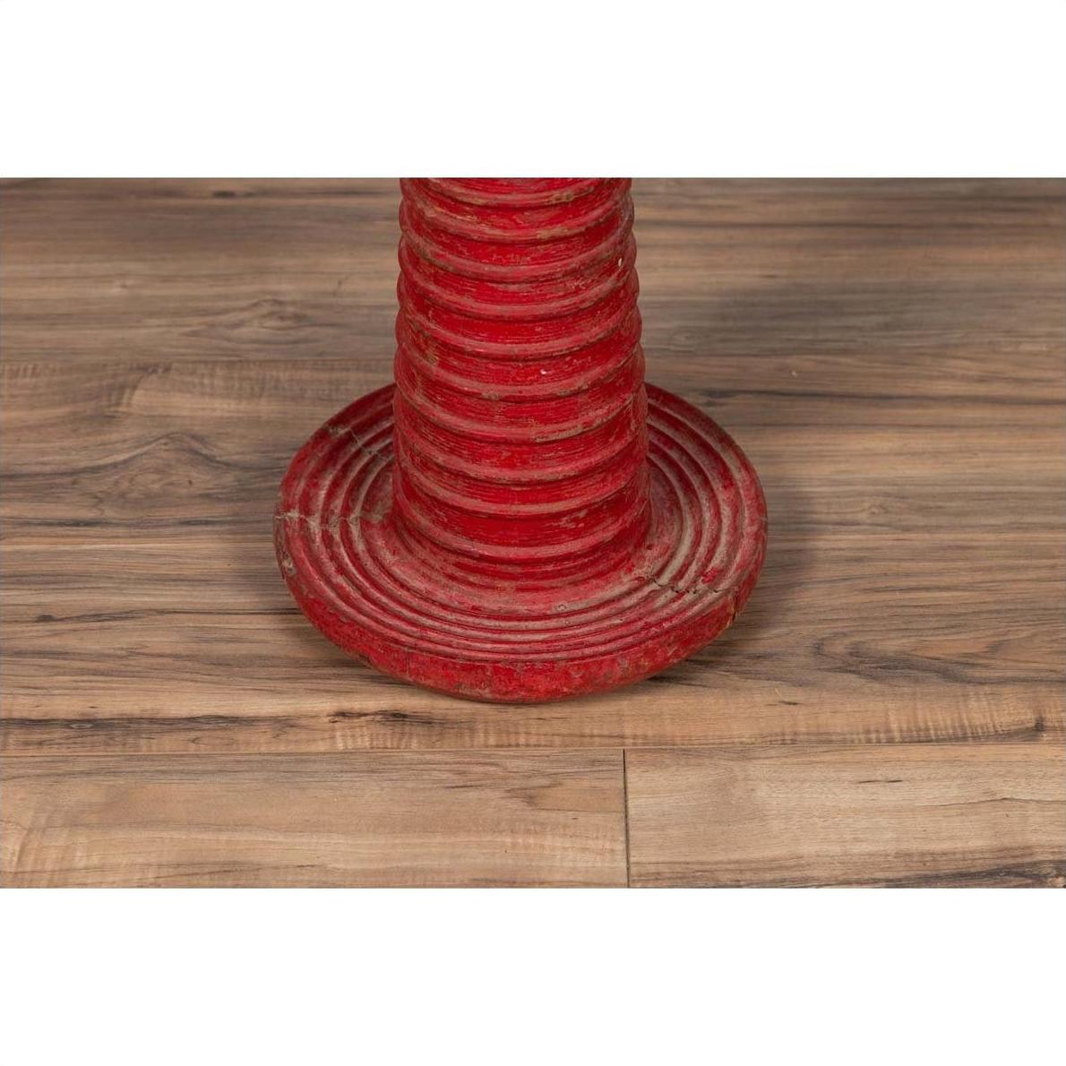 Red wood ceremonial drum with round base on wooden floor, white border in background, indoor setting.