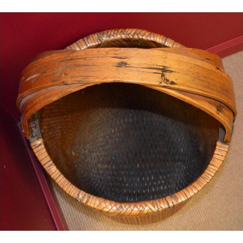 Brown rattan grain basket with wide wooden handle on red and beige background.