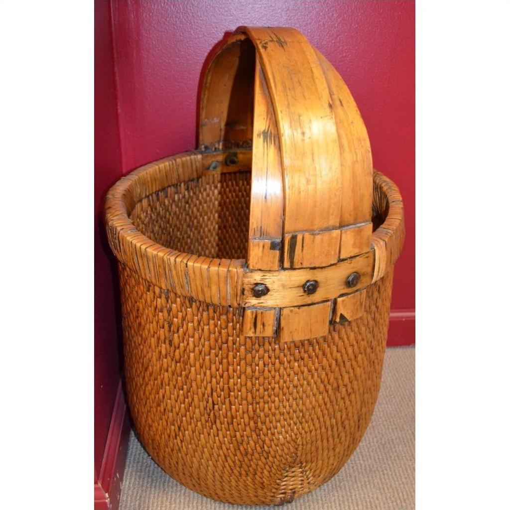 Brown woven rattan grain basket with wooden handle in corner against red and beige walls.