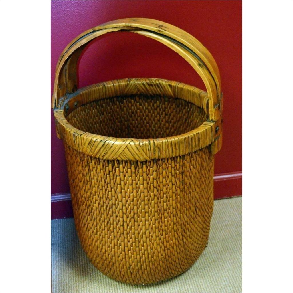 Antique woven rattan grain basket with curved handle on beige carpet, red wall background.