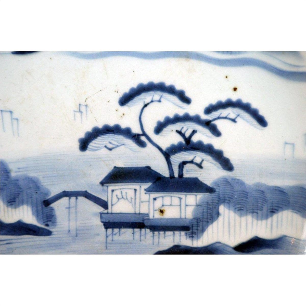 Blue and white porcelain plate with hand painted scene of house by water, trees, and small bridge, Meiji Arita style.