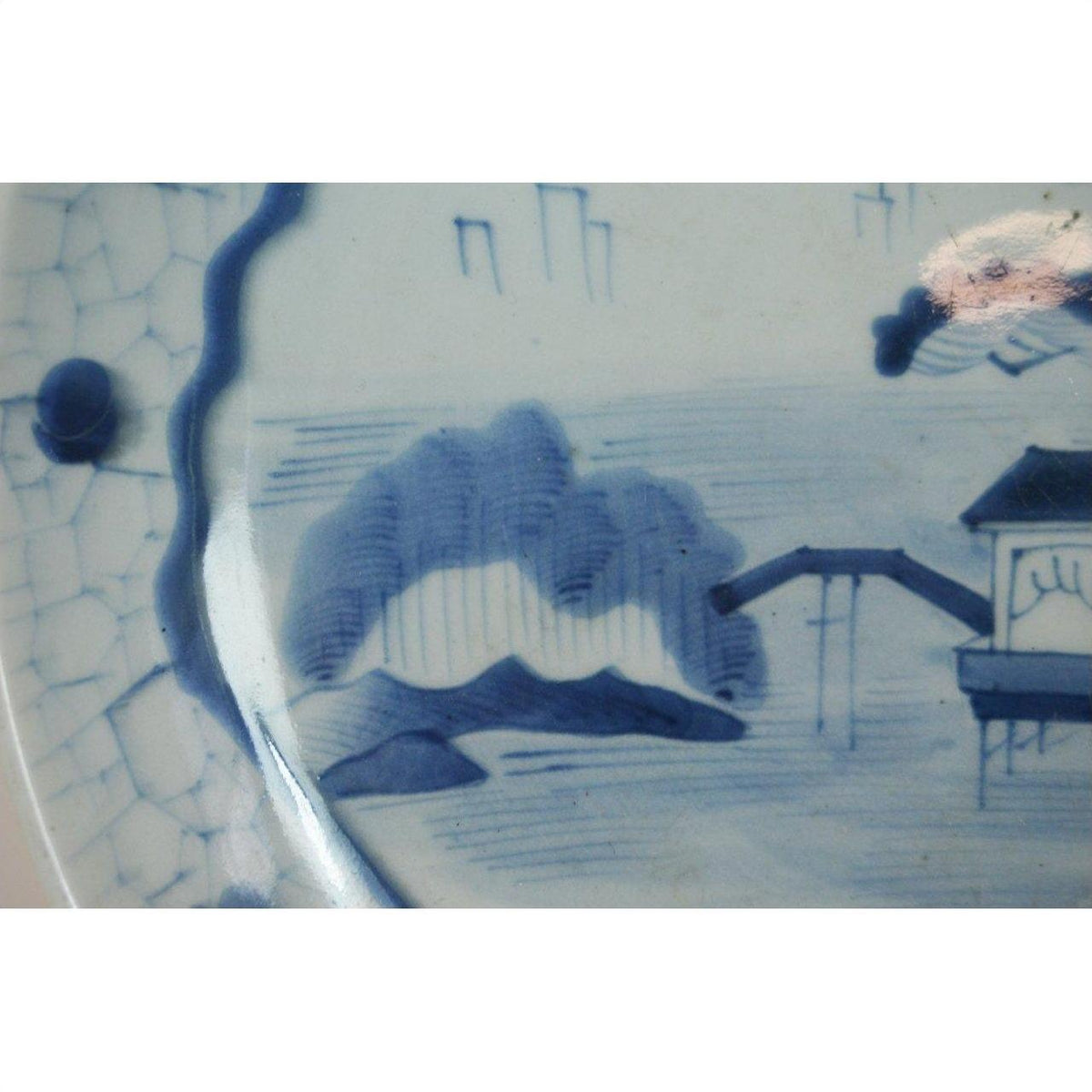 Blue and white porcelain plate with hand painted trees, water, and building in classic Arita Meiji style.