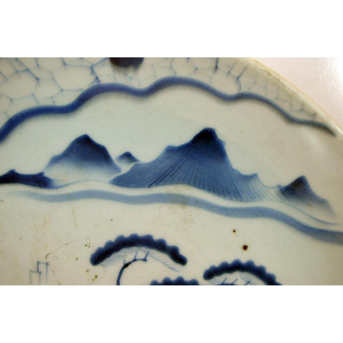 Blue and white ceramic plate with hand-painted mountain landscape motif on rim, Arita Meiji style, close-up.