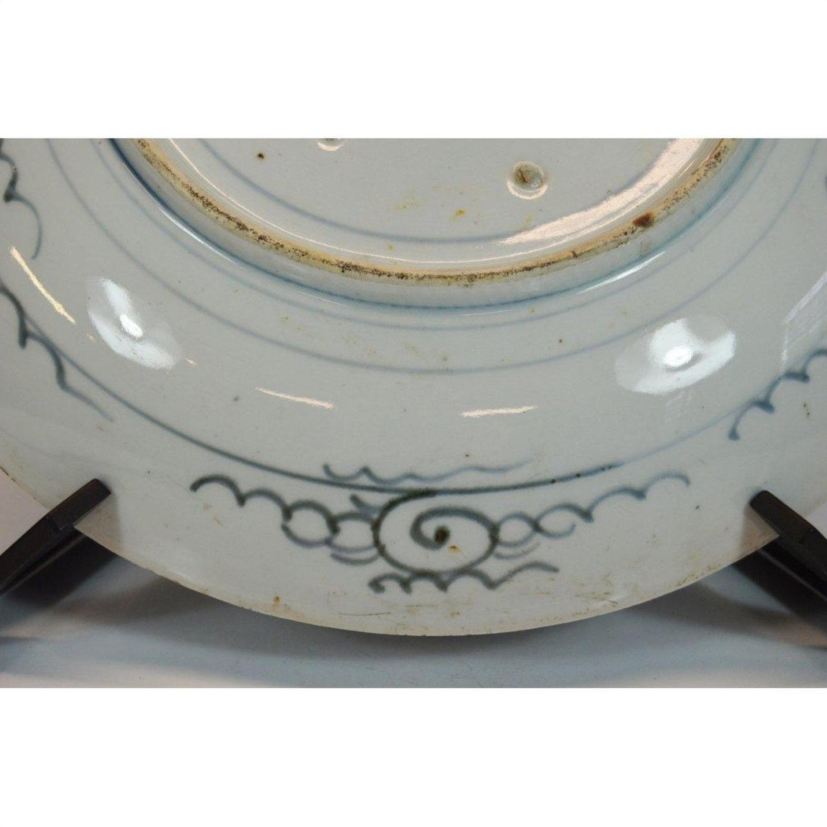 Blue and white ceramic plate close-up, underside view with hand-painted patterns and slight discoloration.