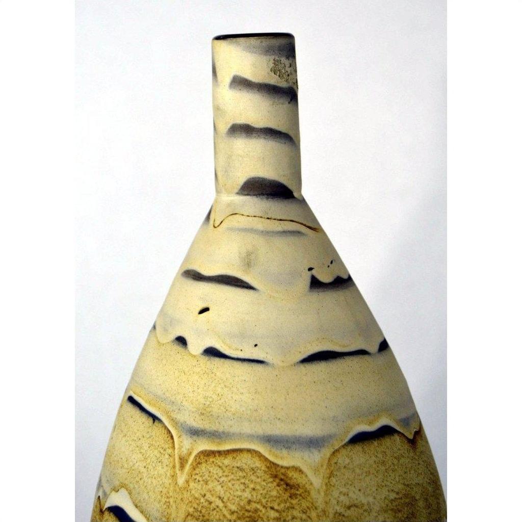 Close-up of a large earth-toned ceramic vase with a tall neck and wavy beige and black sand dune-like lines.