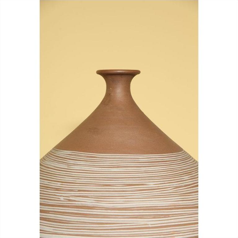 Close-up of a brown hand-made ceramic vase with a narrow neck and white stripes, on a light yellow background.