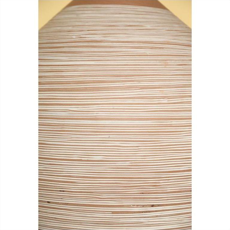 Close-up of light brown ceramic vase with evenly spaced horizontal white lines.