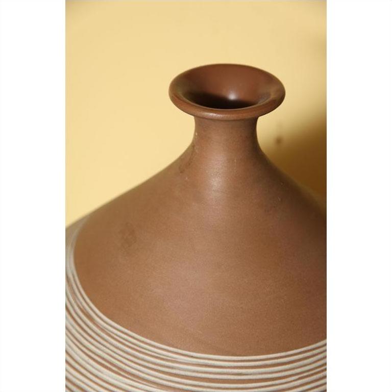 Close-up of a white-striped ceramic vase with a narrow neck, set against a yellow background.
