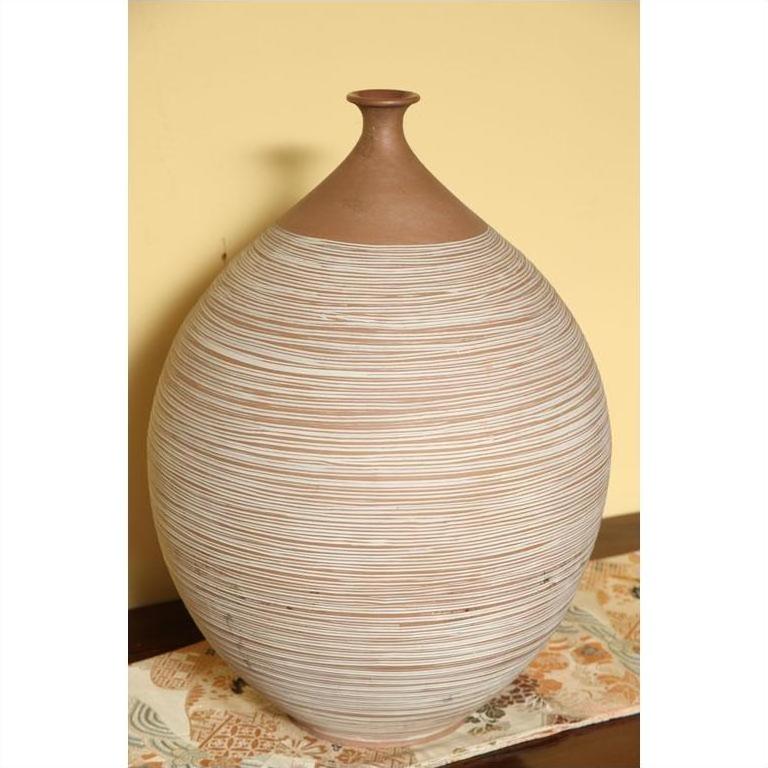 Large ceramic vase with thin stripes on patterned cloth, yellow wall background, indoor setting.