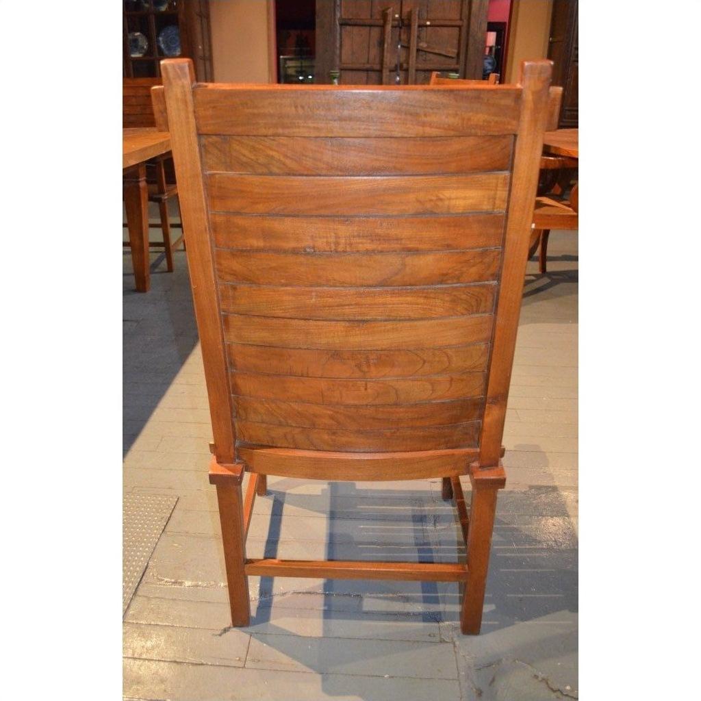 Brown teak armless chair with curved slats, rear view, on a tiled floor.