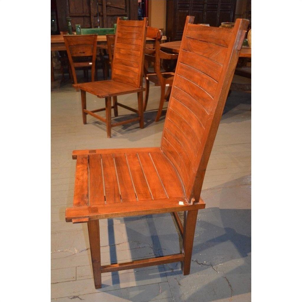Brown wooden Arts &amp; Crafts style armless chair with tall curved slatted back among other chairs and tables.