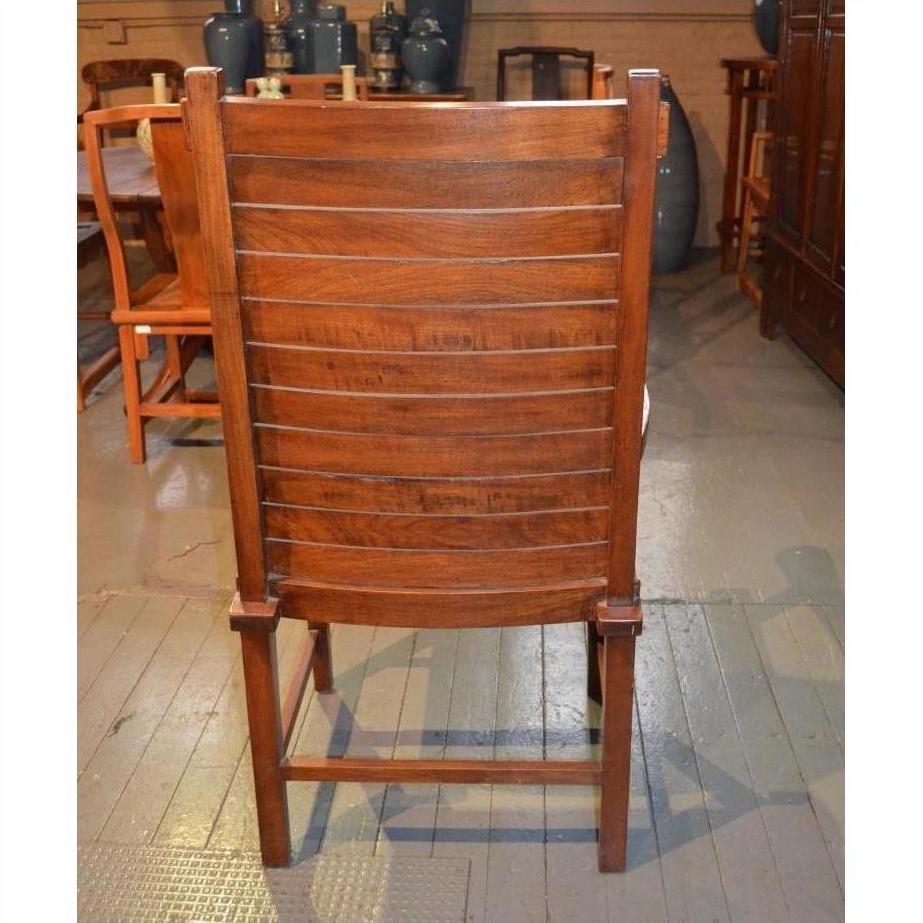 Brown wooden Arts &amp; Crafts style chair with slatted backrest, rear view on wooden floor among other furniture.