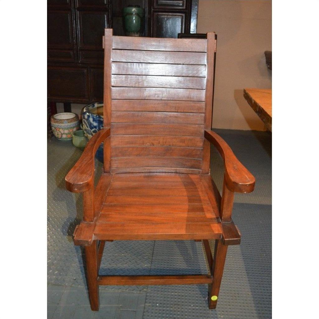 Brown teak armchair with slatted back and seat, Arts &amp; Crafts style, indoors on a patterned floor.