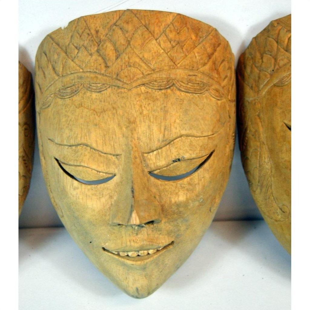 Light wood Balinese dancing mask with delicate carving, closed eyes, and a subtle smile on a light background.