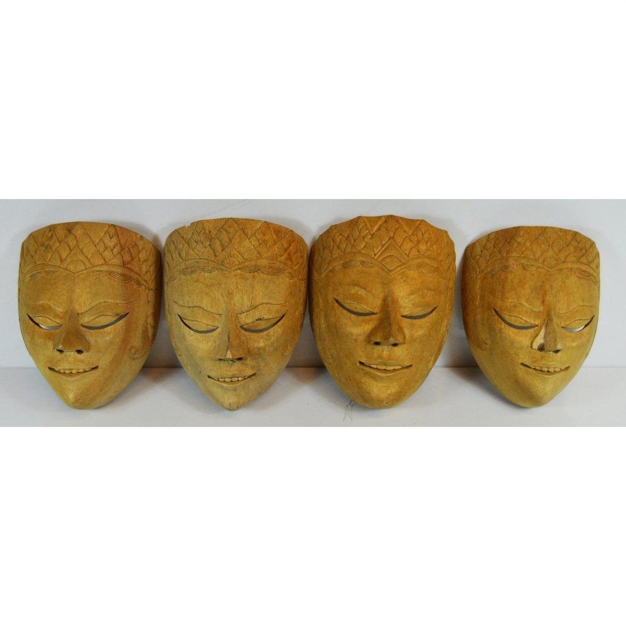 Close-up of four intricately patterned Balinese masks with serene, closed eyes on a white background.