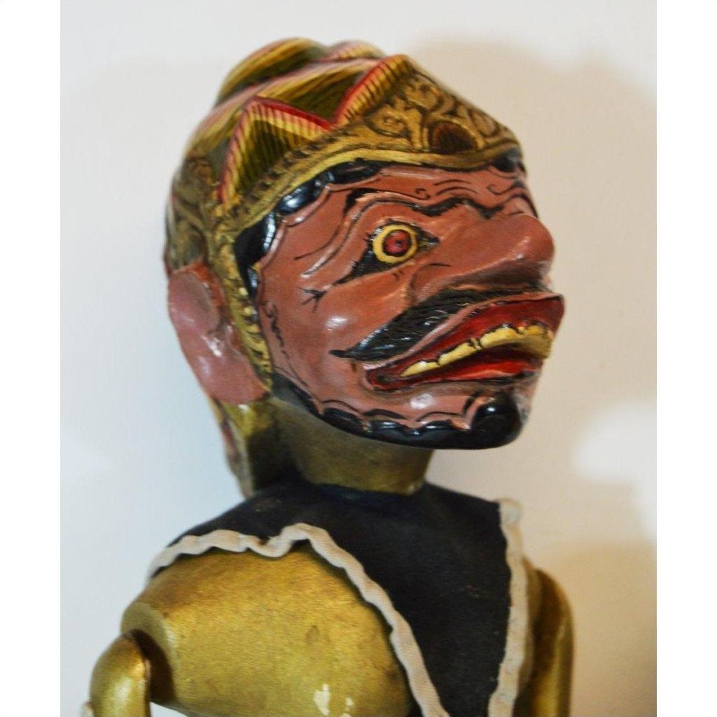 Close-up of hand-carved Balinese puppet with painted face, gold headdress, prominent teeth, black and gold costume.