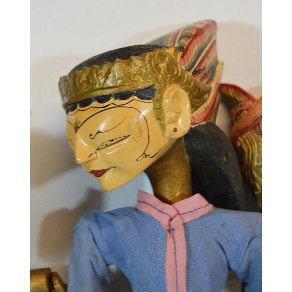 Close-up of a Balinese puppet figure in blue clothing, gold headdress, and painted face detailing.