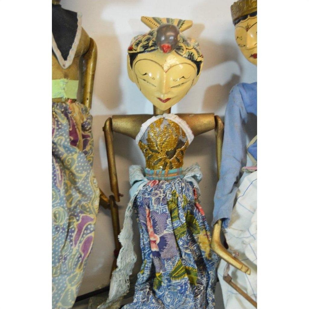 Colorful wooden Balinese puppets with gold headdress, painted faces, and batik clothing, standing indoors.
