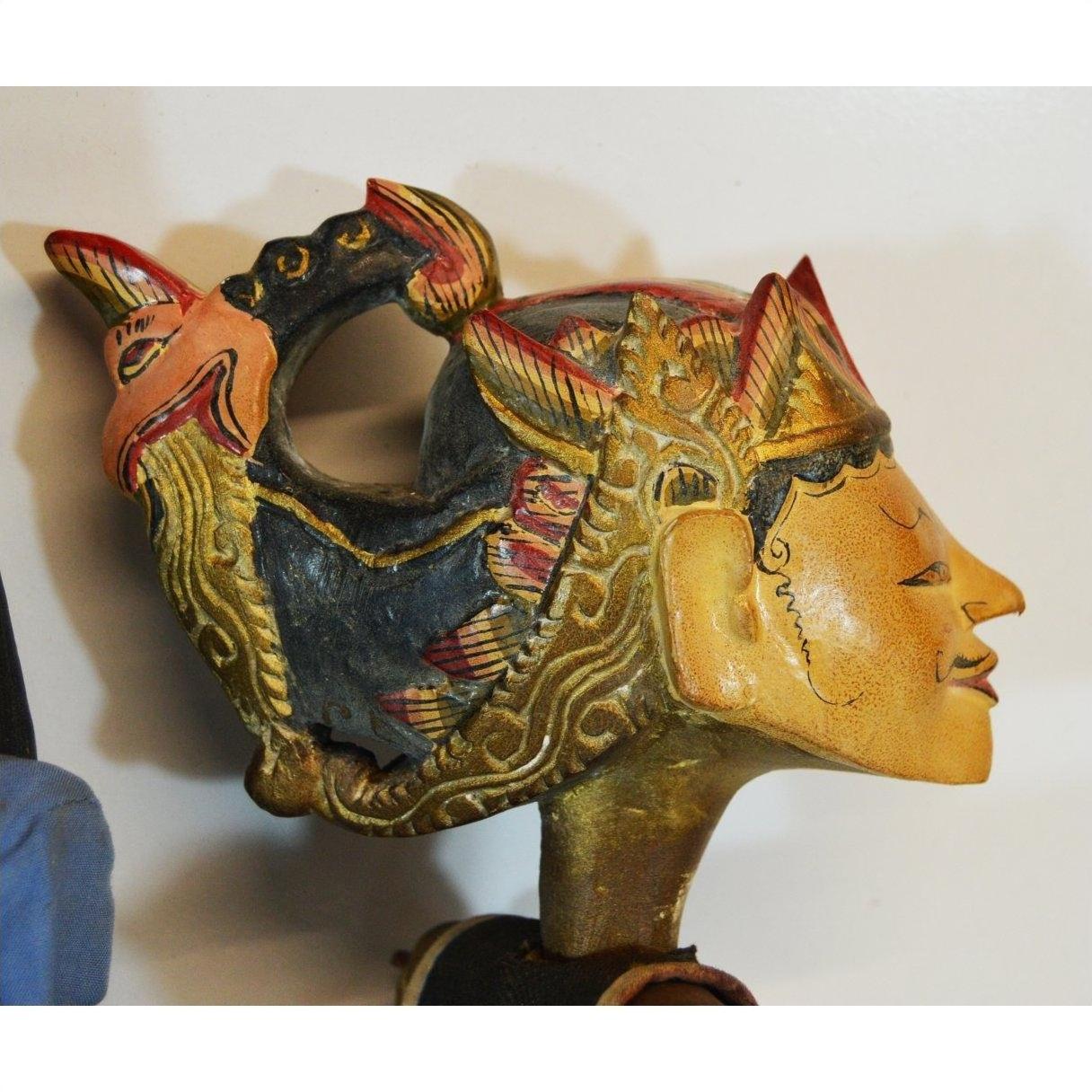 Close-up of a red and gold hand-carved wooden Balinese puppet head with intricate carvings, indoors.