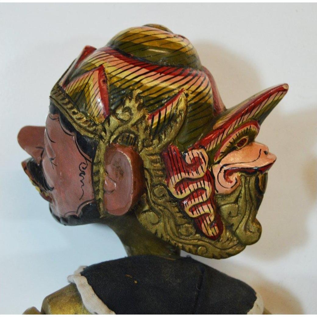 Close-up of a hand-carved wood Balinese puppet head with intricate gold, red, and black traditional carvings.