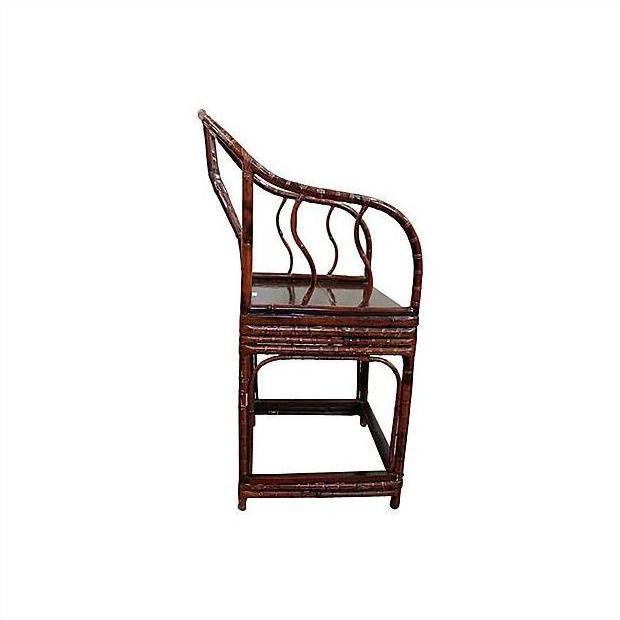 Brown bamboo horseshoe chair with curved backrest and wavy slats, side view, on white background.