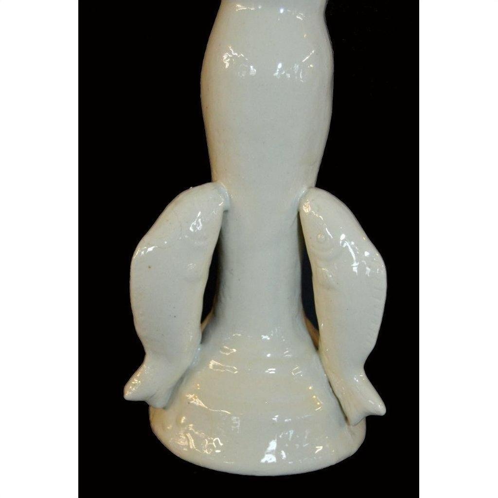 White Blanc de Chine porcelain candle holder with two dolphin figures, close-up on black background.