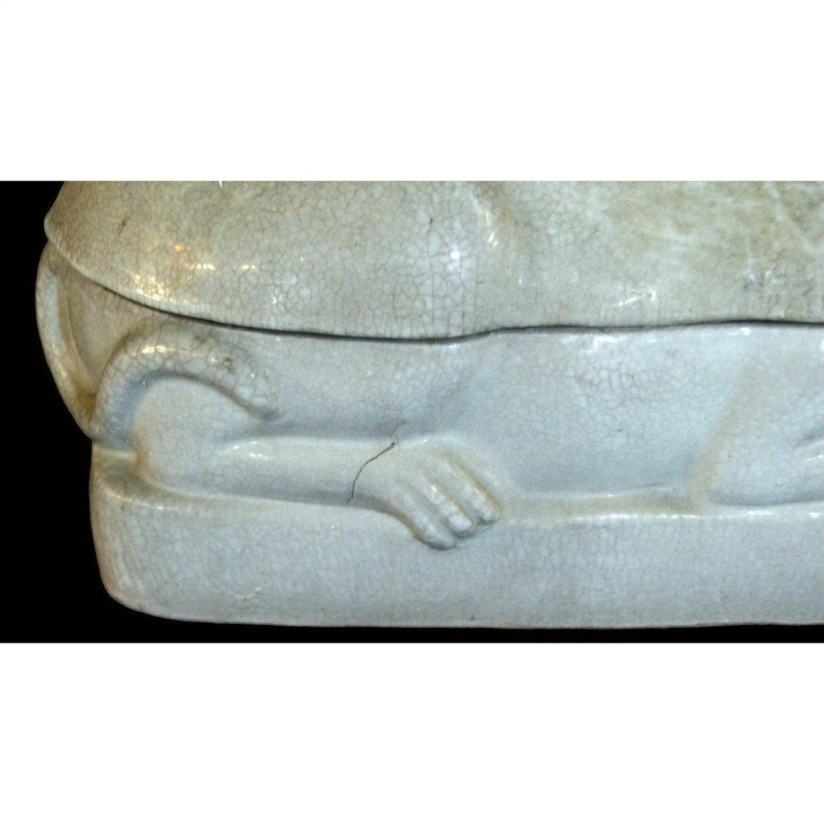 Close-up of white porcelain cat figurine, showing sculpted paw and tail on a rectangular base.