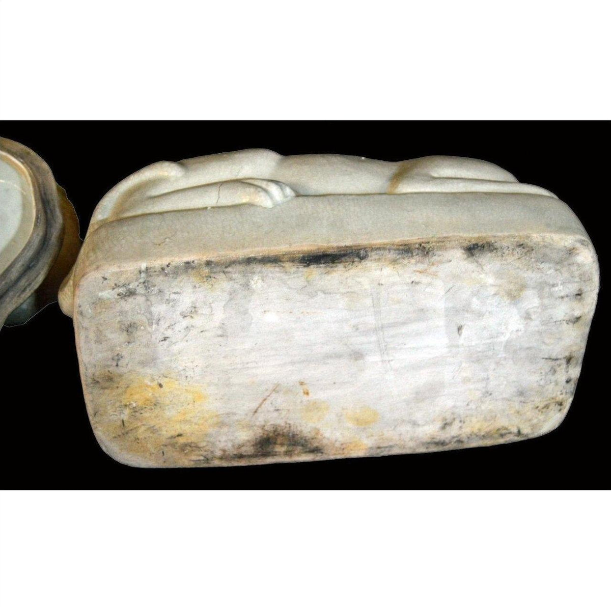 White porcelain cat on a weathered, discolored rectangular base with patina underneath.