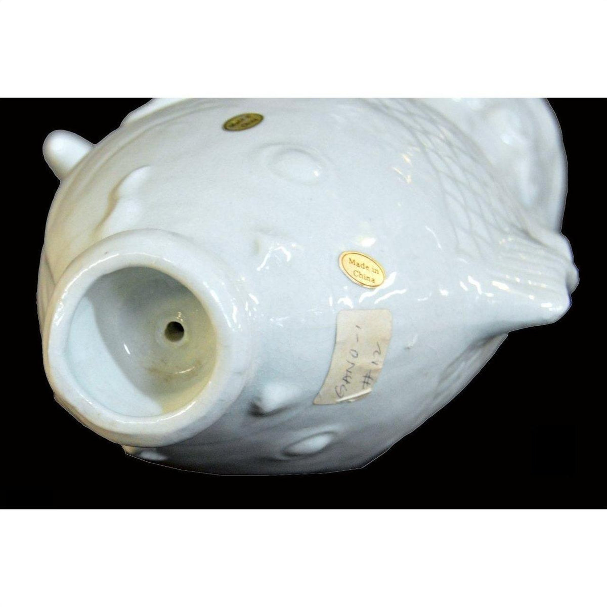 White porcelain fish with two gold stickers, including one reading "Made in China," on a black background.