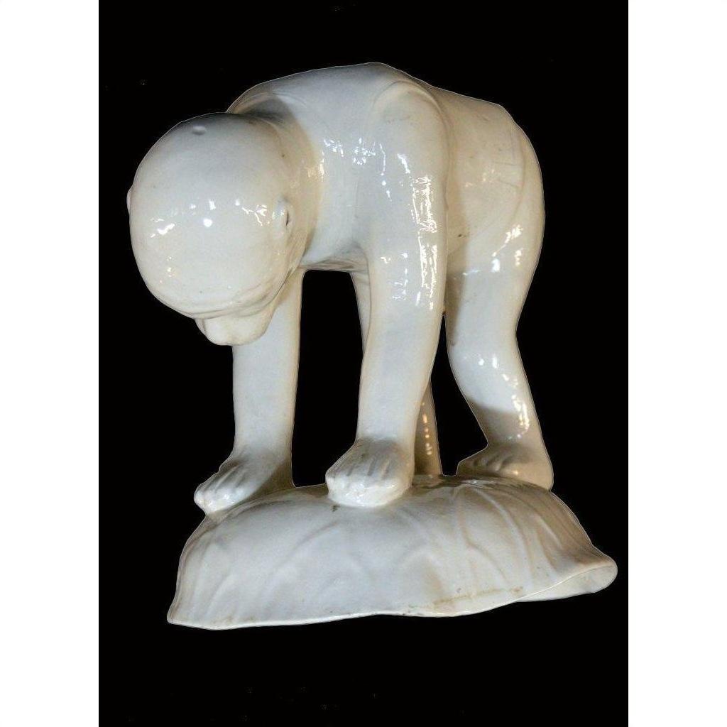 White porcelain monkey sculpture, Blanc de Chine, on hands and feet with head bowed, displayed on a small base.