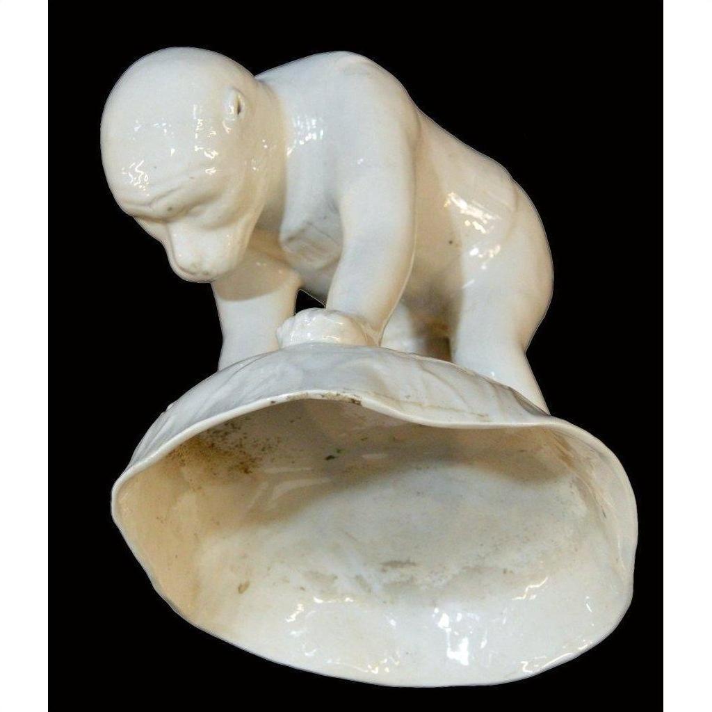 White porcelain monkey holding open shell, Blanc de Chine style, close-up against black background.