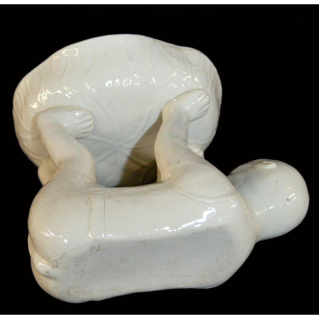 White porcelain monkey lying on back balancing large bowl with raised legs and arms, studio background.