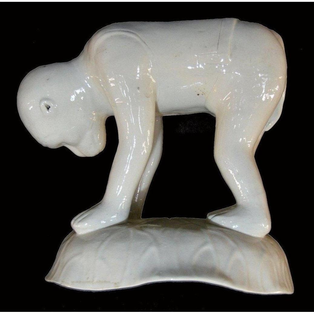 Close-up of white Blanc de Chine porcelain monkey, crouched on textured base against a black background.