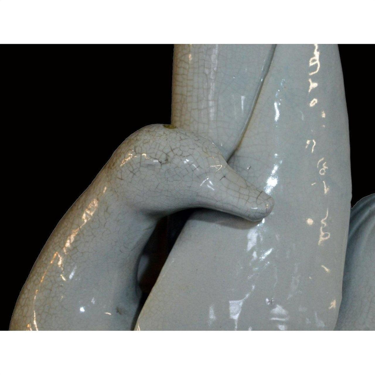 Close-up of glossy light gray porcelain swan head and neck from Blanc de Chine vase against black background.