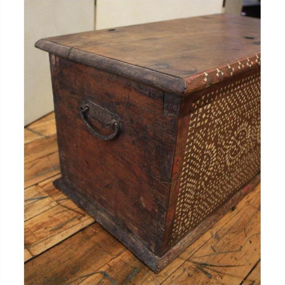 Brown carved Indonesian wood blanket chest on wooden floor.
