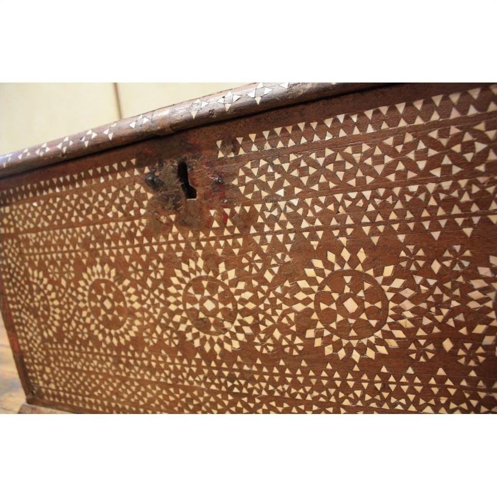 Close-up of a brown wood blanket chest with geometric bone inlay patterns and a metal keyhole.
