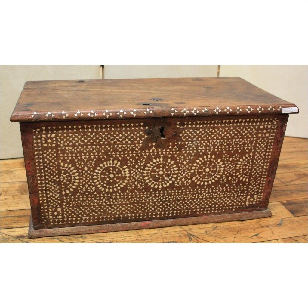 Brown wooden blanket chest with white geometric bone inlay patterns on the front, set on a wooden floor.