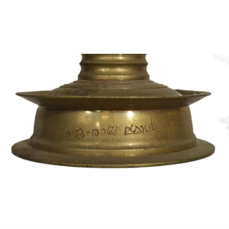 Close-up of brass incense burner with spiral design and engraved Malayalam script, antique-inspired style.