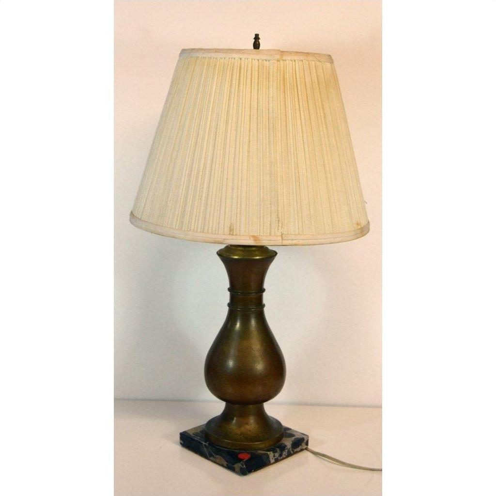 Close-up of brass lamp with pleated beige shade and square marble base, set against a plain background.