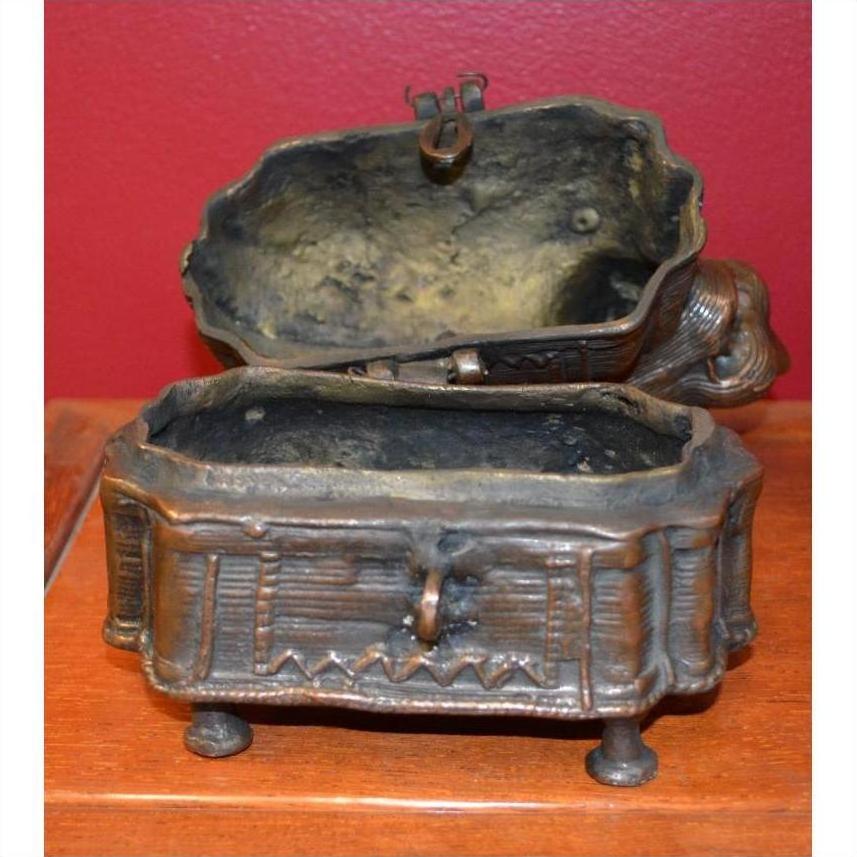 Brass animal-shaped box with legs and hinged lid, open on wood surface, red wall background, close-up.