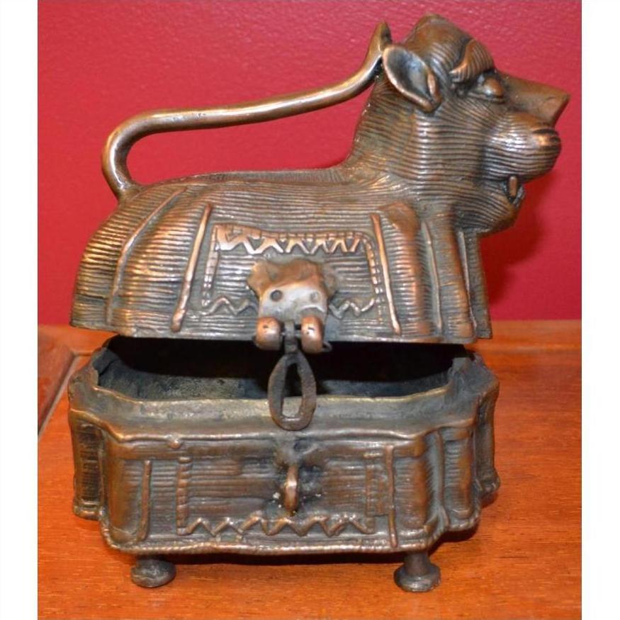 Close-up of brass animal-shaped monkey box with hinged lid slightly open, set against a solid red background.