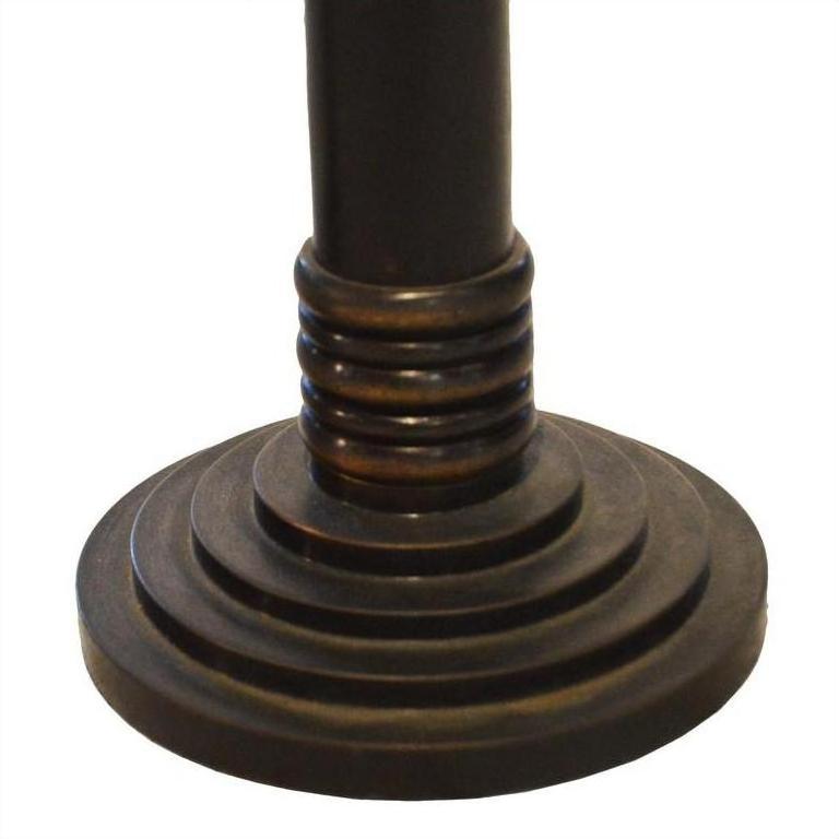 Close-up of bronze metal candle holders with dark, round, tiered bases and concentric rings, vertical pole design.