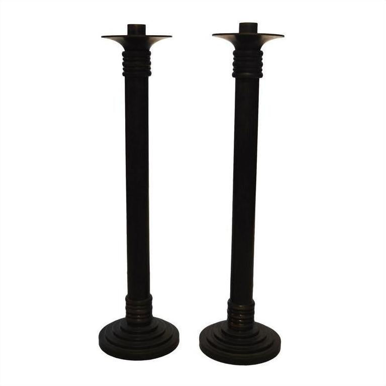 Close-up of two tall black bronze candle holders with round bases and ribbed accents, side by side.