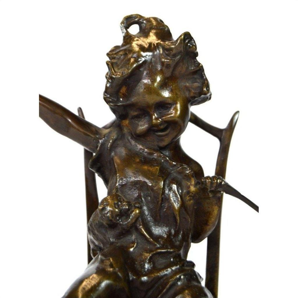 Bronze cherub doll sculpture with detailed smiling face, curly hair, seated holding an object, close-up view.