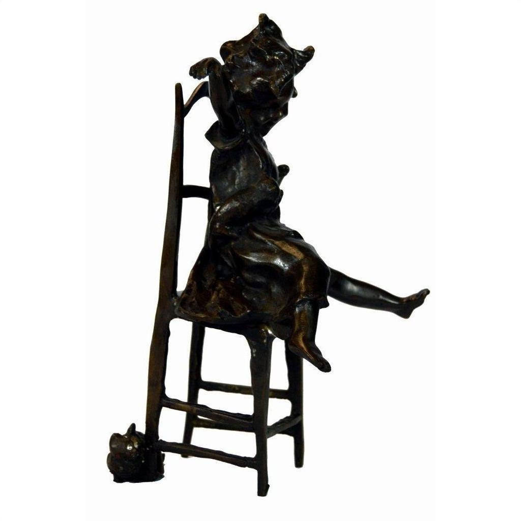 Bronze girl doll sculpture sitting on tall chair with outstretched legs, small cat at base, close-up view.