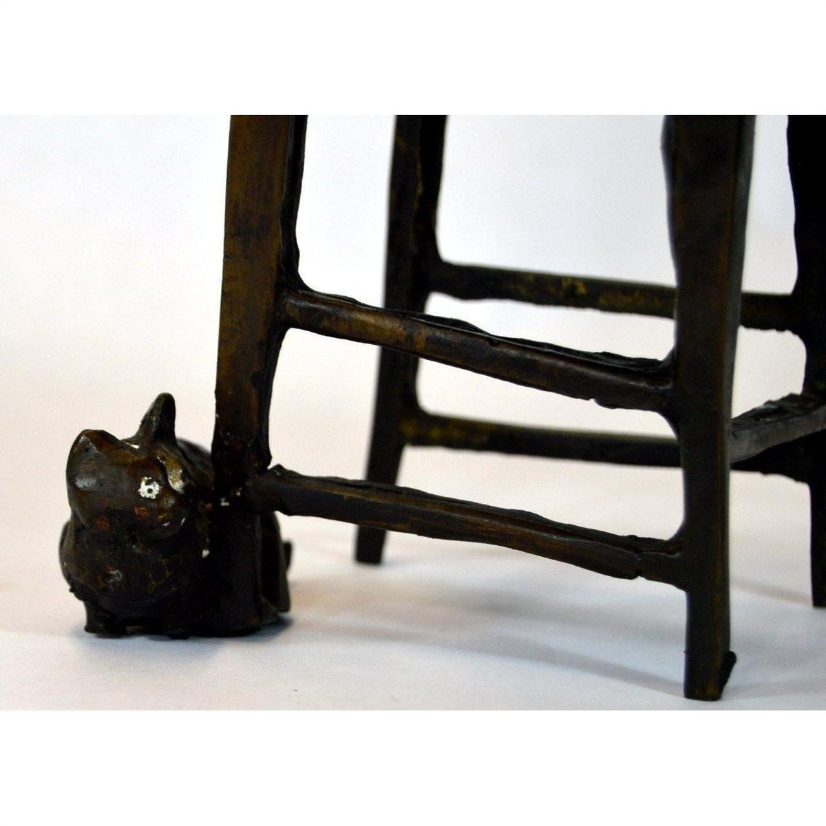 Bronze cat sculpture beside wooden chair legs and rungs, indoors.