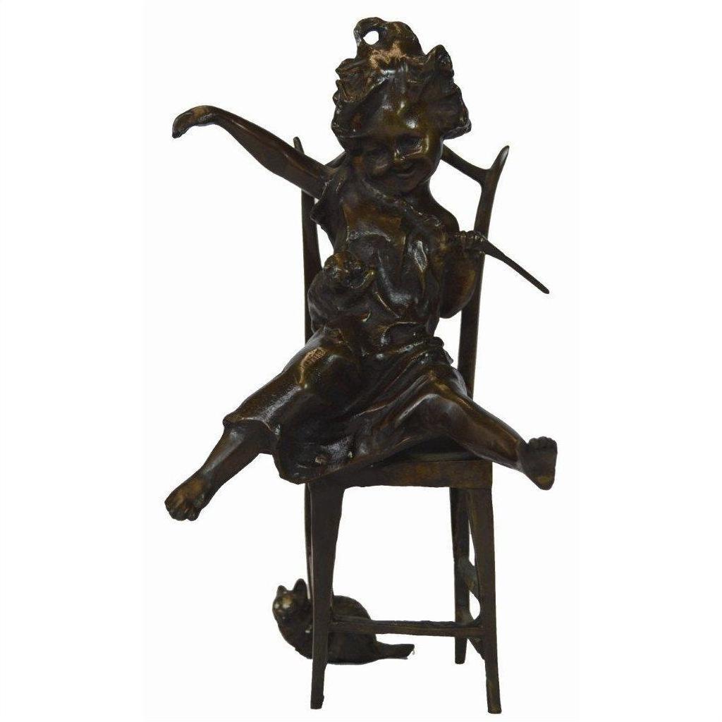Bronze doll of a playful child sitting on chair with a cat in their lap and another cat beside the chair.