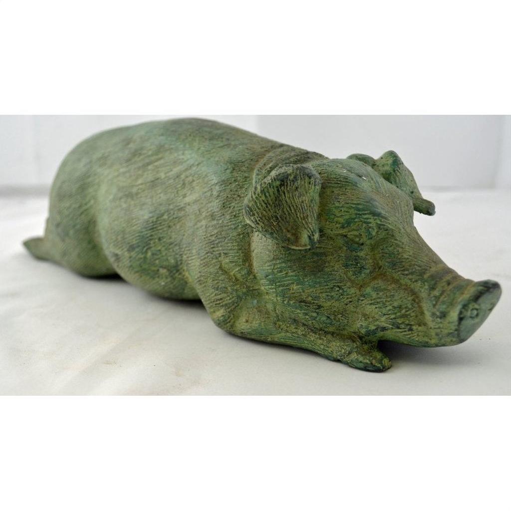 Bronze pig figurine lying down on a white surface, close-up, decorative tabletop object.